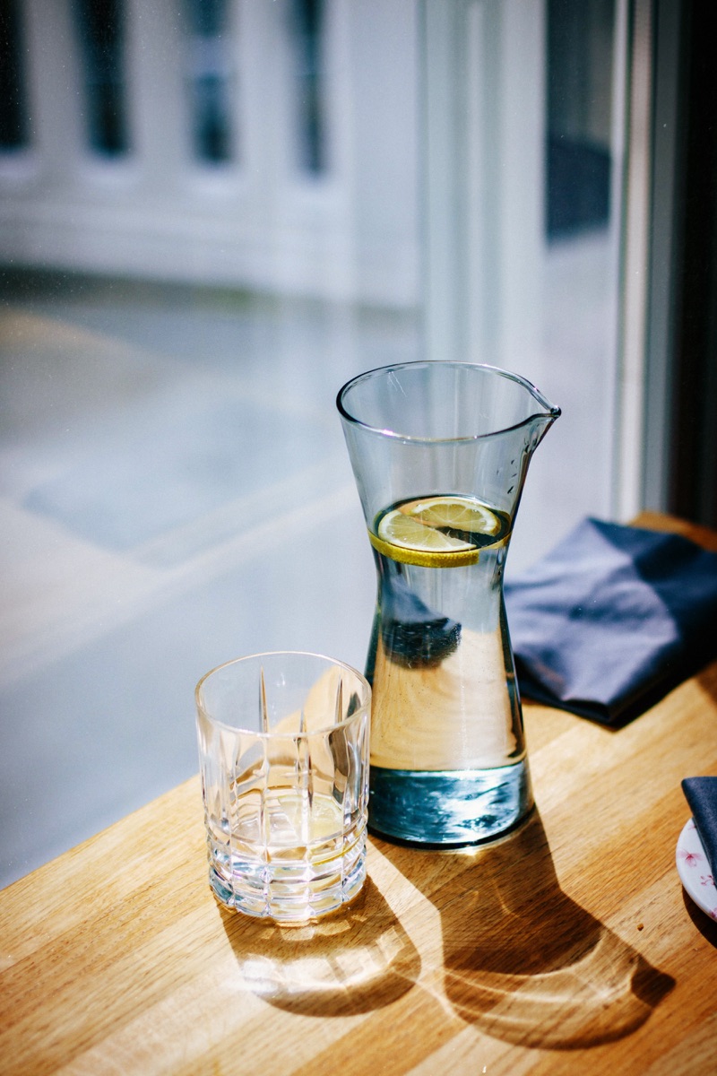Karaffe mit frischem Zitronenwasser und ein Glas auf einem Holztisch am Fenster